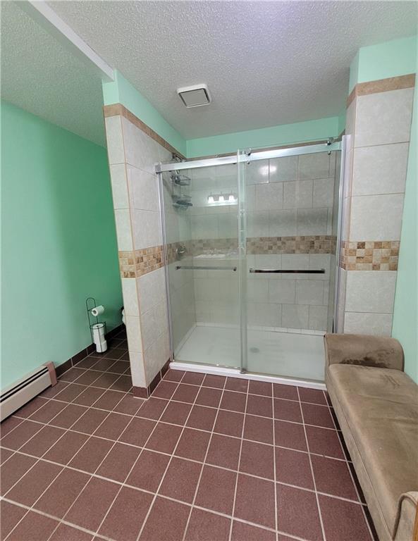 bathroom featuring a shower with door, a baseboard heating unit, tile patterned floors, and a textured ceiling