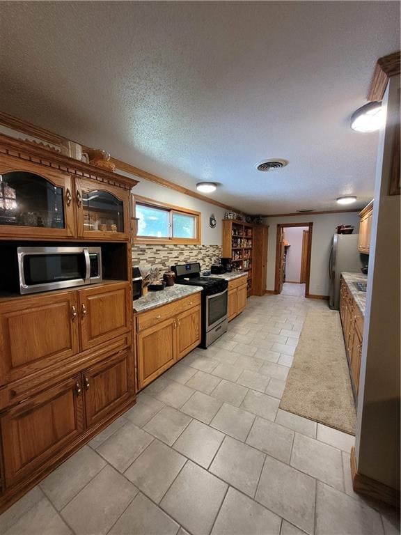 kitchen with light tile patterned floors, a textured ceiling, stainless steel appliances, decorative backsplash, and ornamental molding