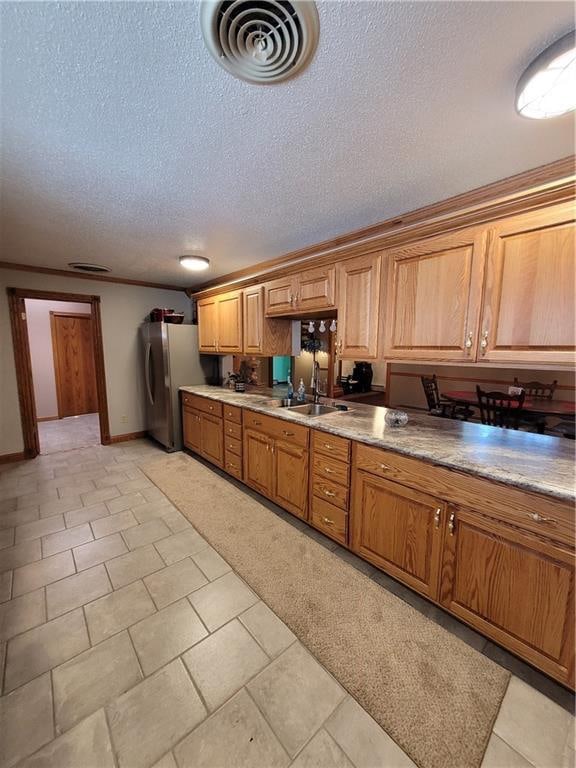 kitchen featuring stainless steel fridge, sink, light tile patterned flooring, and a textured ceiling