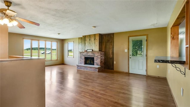 unfurnished living room featuring a textured ceiling, a brick fireplace, wood-type flooring, and ceiling fan