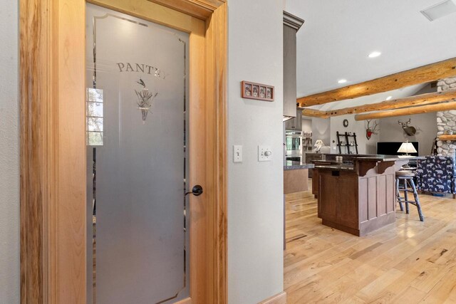 interior space featuring dark countertops, open floor plan, a breakfast bar, beam ceiling, and light wood-style floors