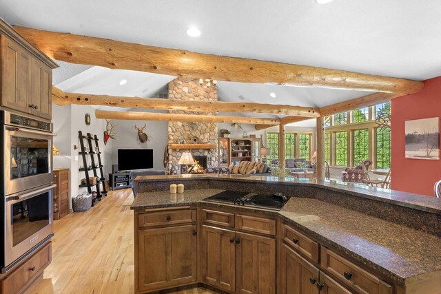 kitchen with open floor plan, electric stovetop, double oven, a stone fireplace, and vaulted ceiling with beams