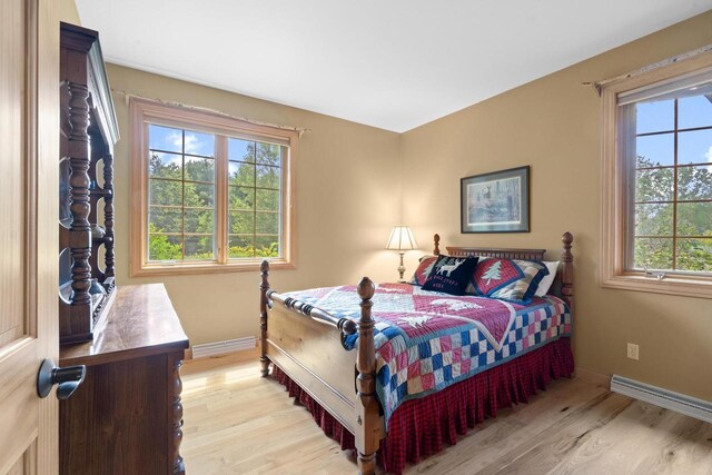 bedroom featuring a baseboard heating unit, light wood-style floors, and baseboards