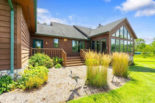 back of property featuring a wooden deck, a yard, and a shingled roof