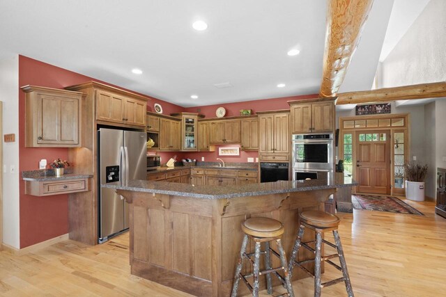 kitchen with a kitchen bar, glass insert cabinets, appliances with stainless steel finishes, and light wood finished floors