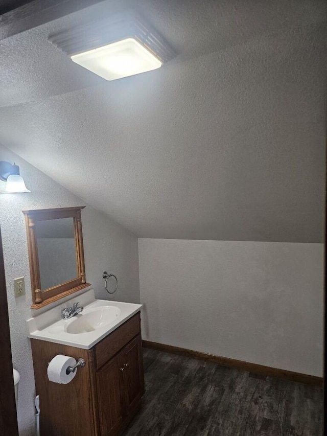 half bathroom with baseboards, vanity, lofted ceiling, wood finished floors, and a textured ceiling