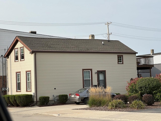 rear view of house with roof with shingles and a chimney