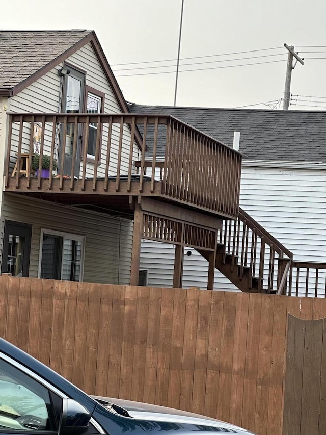 view of home's exterior featuring a shingled roof, a deck, and fence