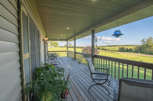 wooden terrace with a lawn, a rural view, and a porch