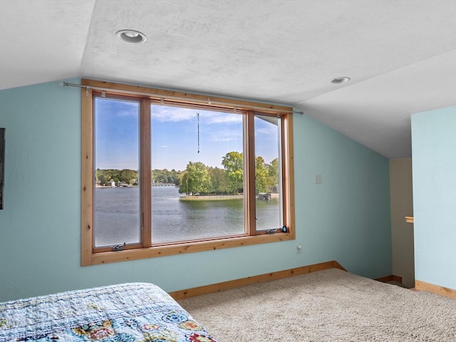 bedroom featuring lofted ceiling, a water view, a textured ceiling, and light colored carpet