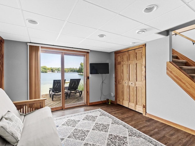 living room featuring a drop ceiling, baseboards, dark wood-style floors, and stairs