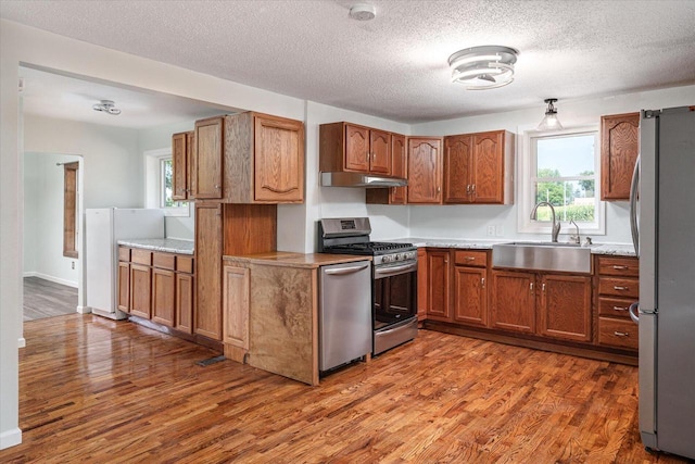 kitchen with hardwood / wood-style floors, appliances with stainless steel finishes, a textured ceiling, and sink