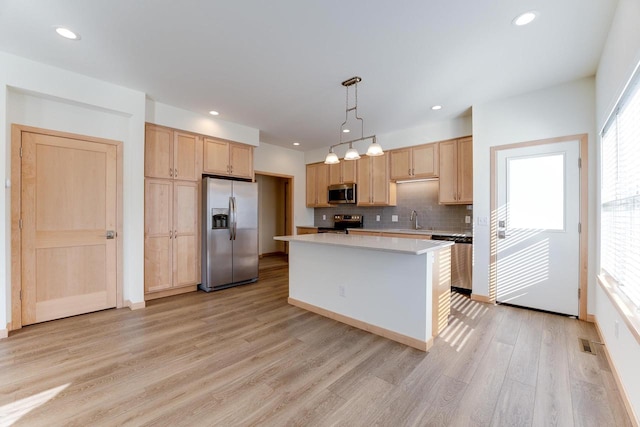 kitchen with pendant lighting, a center island, stainless steel appliances, sink, and light wood-type flooring