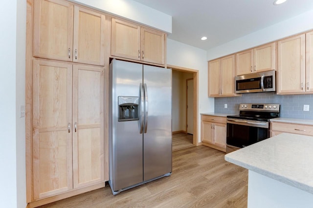 kitchen featuring light wood-type flooring, appliances with stainless steel finishes, decorative backsplash, and light brown cabinetry