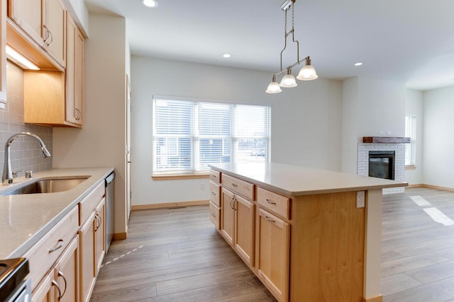 kitchen featuring a center island, a fireplace, light wood-type flooring, sink, and pendant lighting