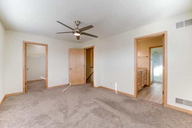 unfurnished bedroom with light carpet, connected bathroom, ceiling fan, a closet, and a walk in closet