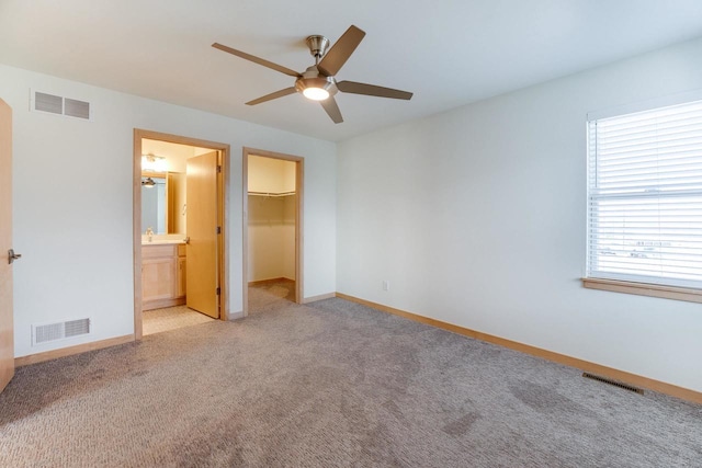 unfurnished bedroom with light carpet, a walk in closet, a closet, ceiling fan, and connected bathroom