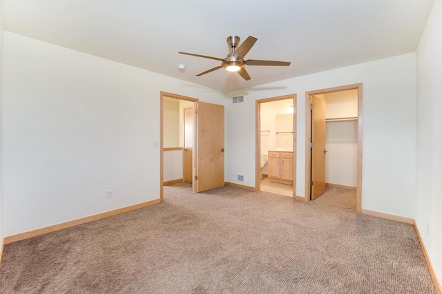 unfurnished bedroom featuring light colored carpet, a walk in closet, a closet, ceiling fan, and connected bathroom