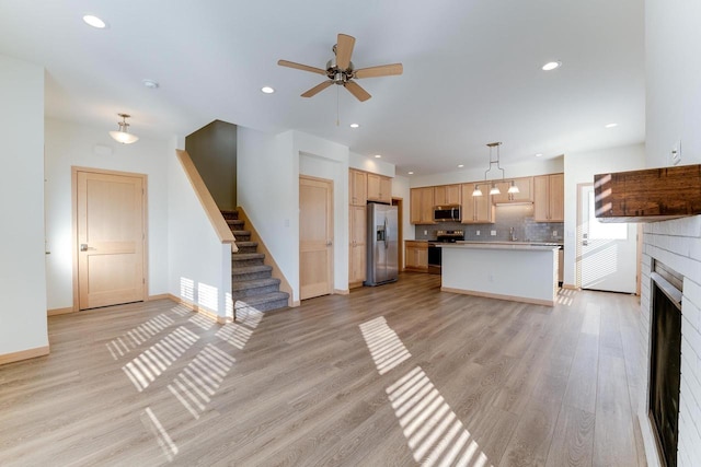 interior space with a fireplace, appliances with stainless steel finishes, light hardwood / wood-style floors, ceiling fan, and pendant lighting