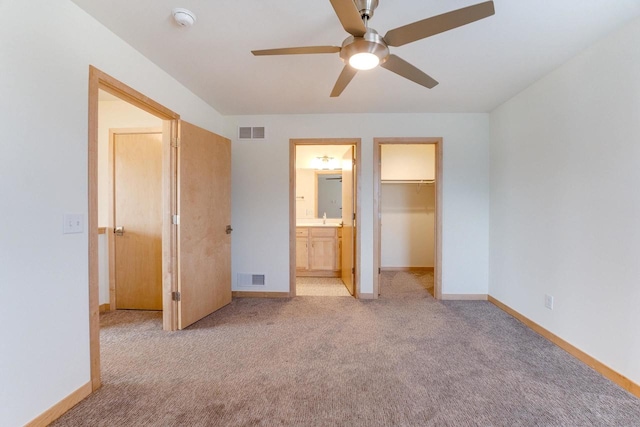 unfurnished bedroom featuring a spacious closet, a closet, ensuite bathroom, light colored carpet, and ceiling fan