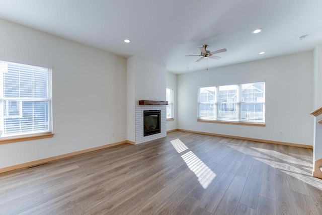 unfurnished living room featuring ceiling fan, light wood-type flooring, and a brick fireplace