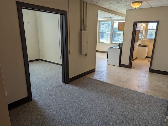 hall featuring electric panel, baseboards, a drop ceiling, and light carpet