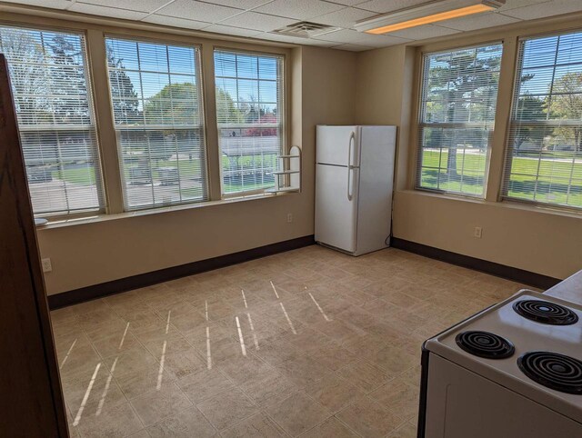 interior space featuring white appliances, a healthy amount of sunlight, and a drop ceiling