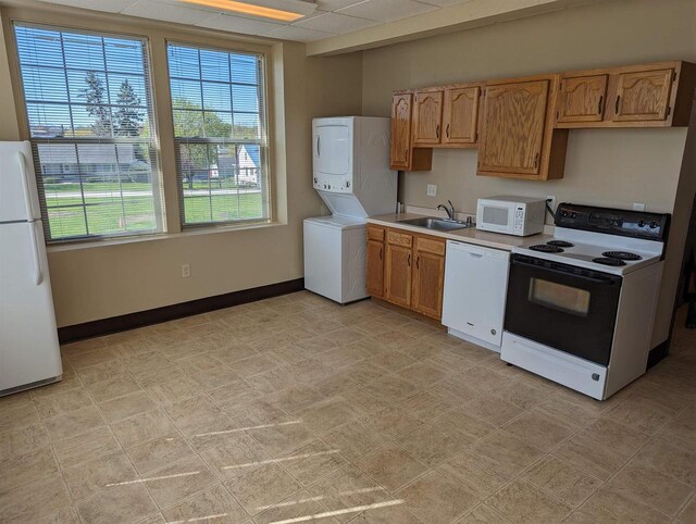 kitchen with stacked washer / dryer, white appliances, sink, and a drop ceiling