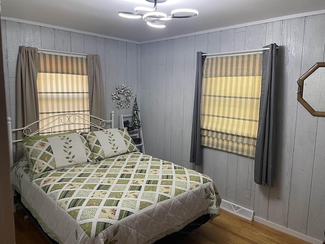 bedroom with a notable chandelier, hardwood / wood-style floors, and wooden walls