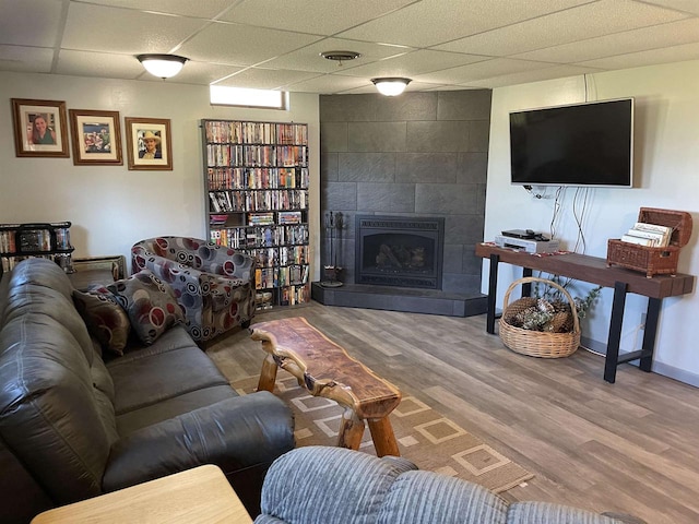 living room with hardwood / wood-style floors, a tile fireplace, and a drop ceiling