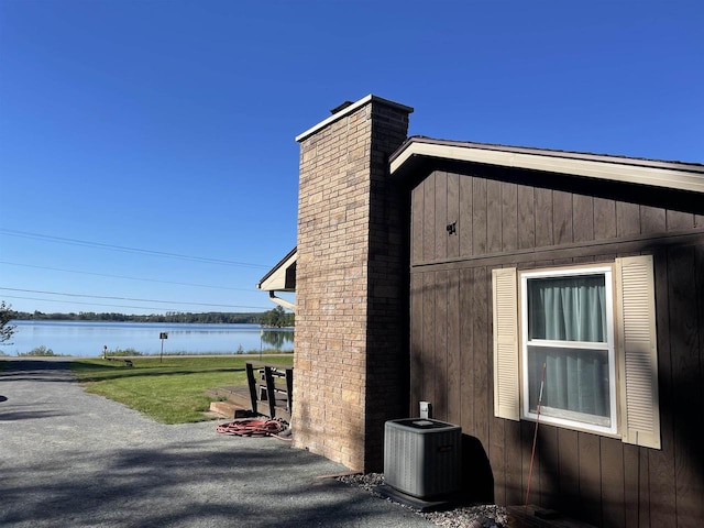 view of side of property with a water view, a lawn, a patio area, and central air condition unit