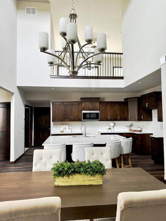 kitchen with a towering ceiling, dark wood-type flooring, dark brown cabinets, and a center island with sink