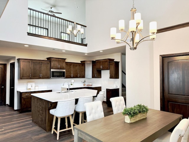 kitchen with ceiling fan with notable chandelier, sink, dark hardwood / wood-style floors, an island with sink, and a high ceiling