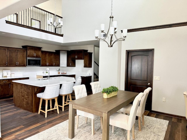 dining space with a towering ceiling, dark wood-type flooring, sink, and a notable chandelier