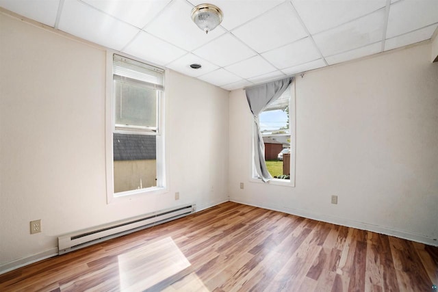 empty room featuring hardwood / wood-style floors, a baseboard radiator, and a paneled ceiling