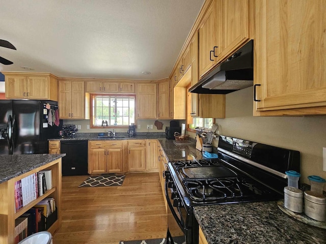 kitchen featuring dark stone countertops, light hardwood / wood-style flooring, black appliances, and sink