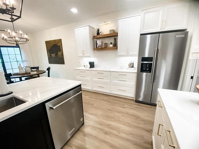 kitchen with light wood finished floors, open shelves, appliances with stainless steel finishes, white cabinetry, and a notable chandelier