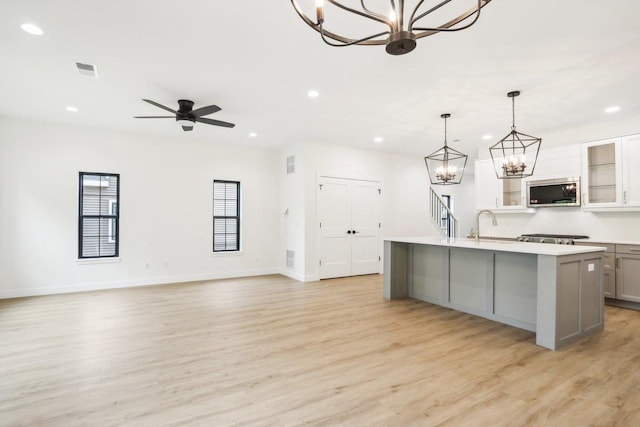 kitchen with a center island with sink, light wood-type flooring, gray cabinets, pendant lighting, and ceiling fan