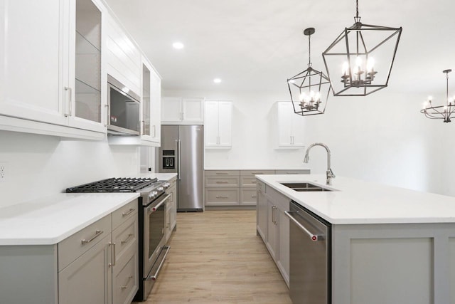 kitchen with an island with sink, gray cabinets, a sink, premium appliances, and glass insert cabinets