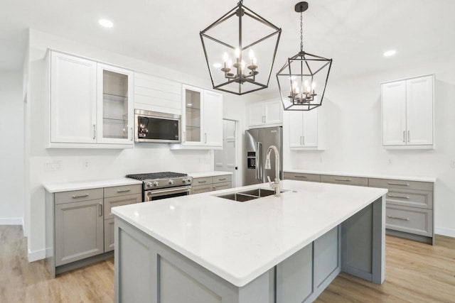 kitchen with a sink, gray cabinetry, appliances with stainless steel finishes, light wood-style floors, and a kitchen island with sink