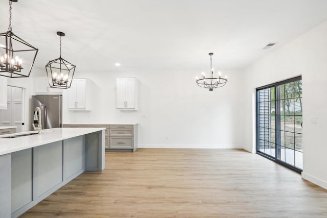 kitchen featuring a sink, a notable chandelier, light wood-style flooring, and stainless steel refrigerator