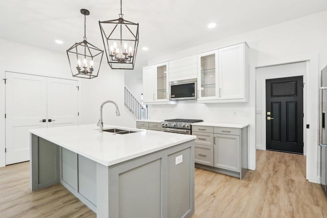 kitchen with a kitchen island with sink, light wood-style flooring, a sink, appliances with stainless steel finishes, and light countertops