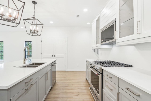 kitchen featuring gray cabinetry, decorative light fixtures, light countertops, appliances with stainless steel finishes, and a sink