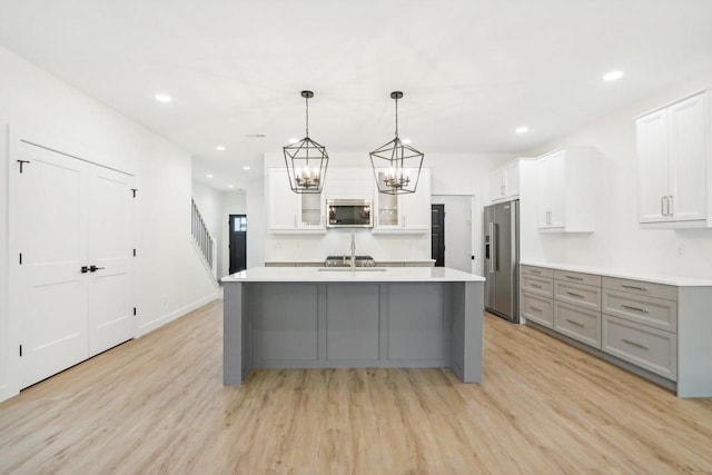 kitchen featuring light wood finished floors, a center island with sink, light countertops, gray cabinets, and appliances with stainless steel finishes