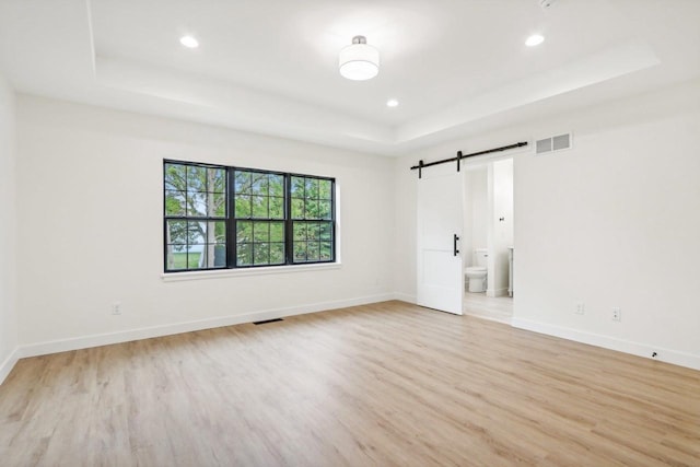 unfurnished room featuring visible vents, baseboards, light wood-type flooring, a barn door, and a tray ceiling