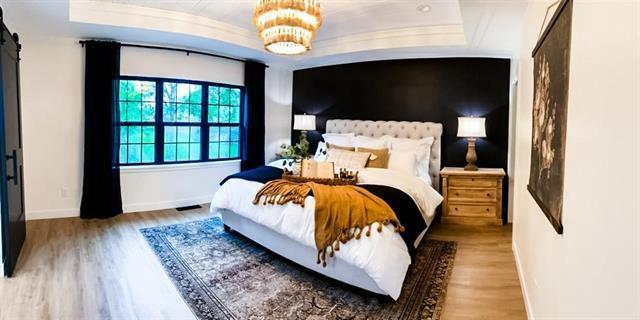 bedroom featuring baseboards, a raised ceiling, a barn door, and wood finished floors