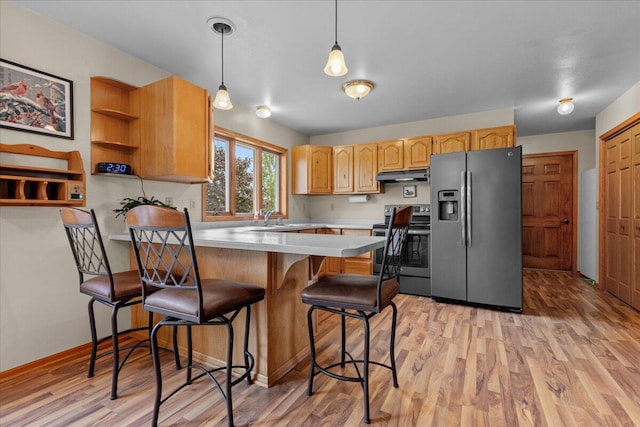 kitchen featuring under cabinet range hood, light countertops, light wood-style flooring, appliances with stainless steel finishes, and a peninsula