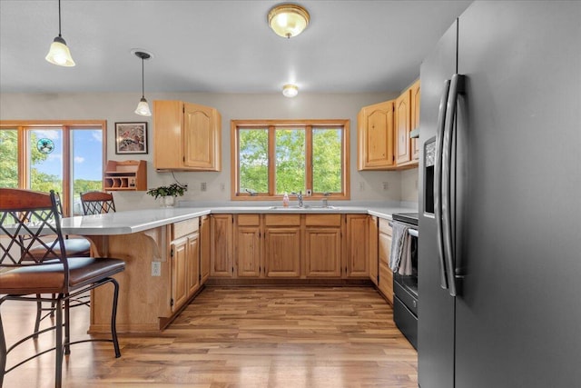 kitchen featuring electric range, stainless steel refrigerator with ice dispenser, light brown cabinets, a sink, and a peninsula