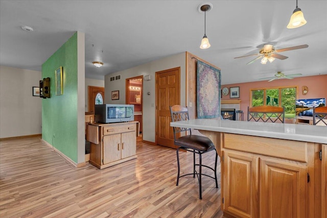 kitchen with visible vents, light wood-style flooring, a warm lit fireplace, stainless steel microwave, and decorative light fixtures