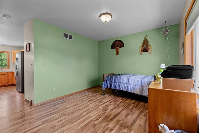 bedroom featuring light wood finished floors, baseboards, visible vents, and freestanding refrigerator